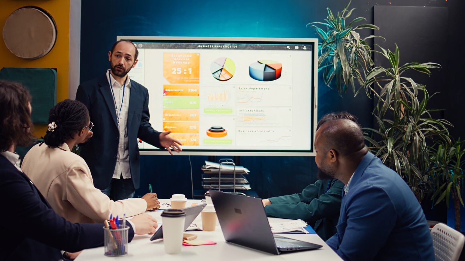 Management consultant gathering his employees for a status update meeting in boardroom, interactive presentation with the latest data. Success metrics and key performance indicators. Camera B.